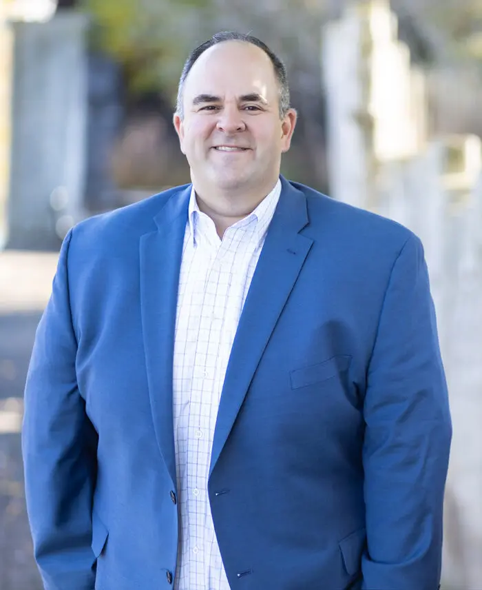 A man in a blue blazer and white checkered shirt smiles outdoors, reflecting Smarter Media's strategic expertise in Fairport, NY.