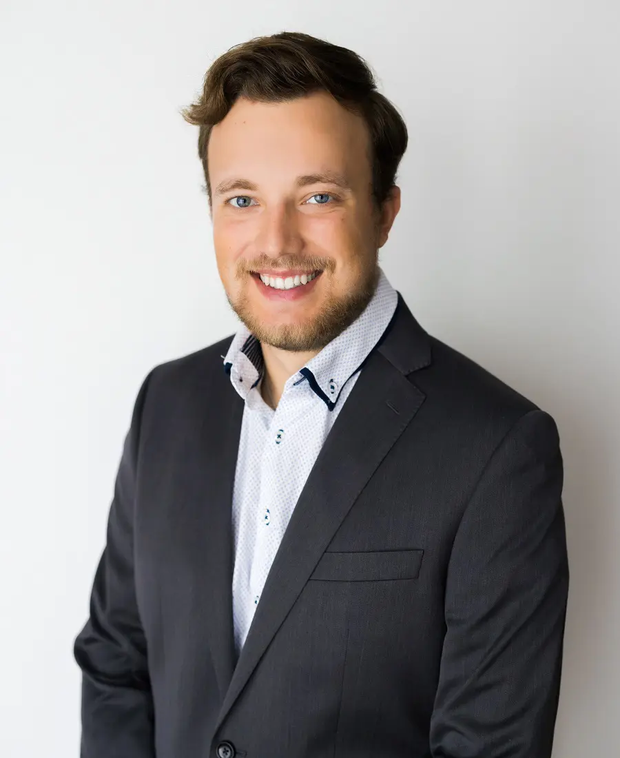 A smiling man with brown hair, blue eyes, a dark suit, and patterned shirt stands before a white backdrop; Fairport, NY professional.
