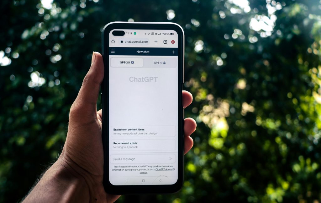 A person holds a smartphone with the ChatGPT conversation page open; lush greenery is blurred behind, reflecting Smarter Media’s innovative approach.
